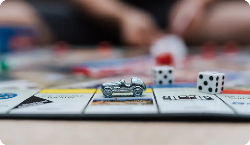 Een scène uit een bordspel met een autofiguurtje en dobbelstenen op een vakje, die de beurtgebaseerde gameplay, verplaatsingen en strategische beslissingen in een bordspel weergeeft